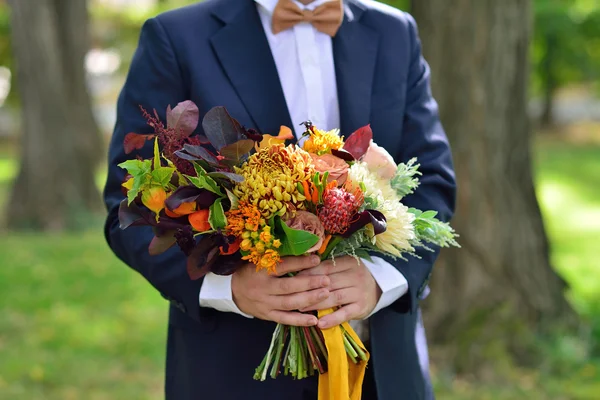Brudgummen i blå kostym innehar en höst bröllop bukett — Stockfoto