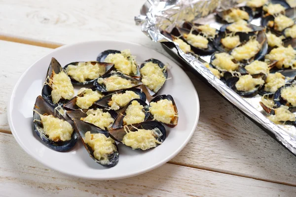 Assiette aux moules cuites au four avec fromage et oignons sur un boisé blanc — Photo