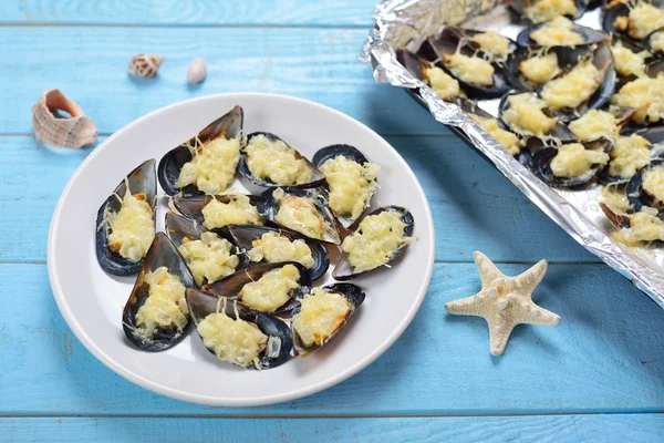 Teller mit gebackenen Miesmuscheln mit Käse und Zwiebeln auf blauem Holz — Stockfoto