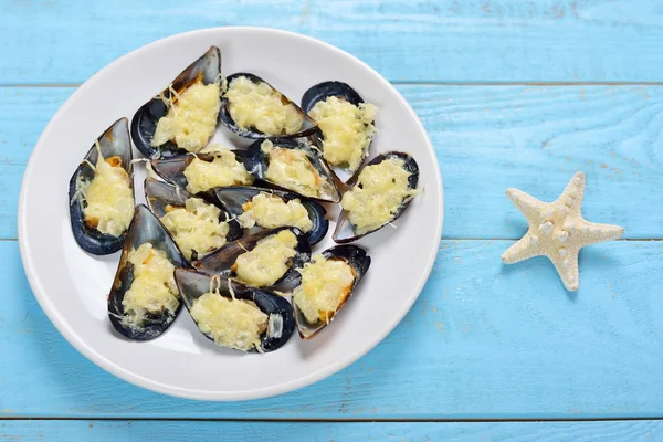 Teller mit gebackenen Miesmuscheln mit Käse und Zwiebeln auf blauem Holz — Stockfoto