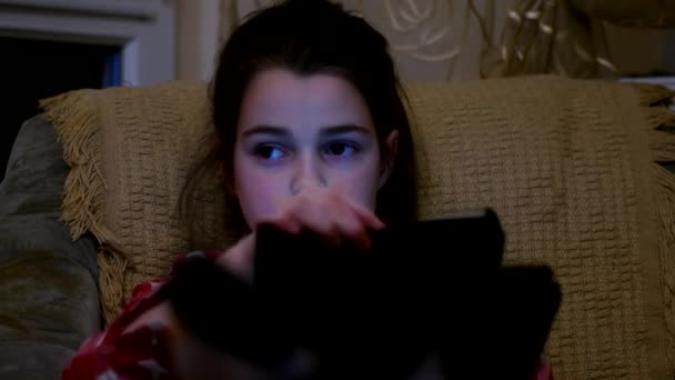 Νεαρό κορίτσι χρησιμοποιώντας μια ταμπλέτα που κάθεται σε έναν καναπέ στο δωμάτιο — Αρχείο Βίντεο