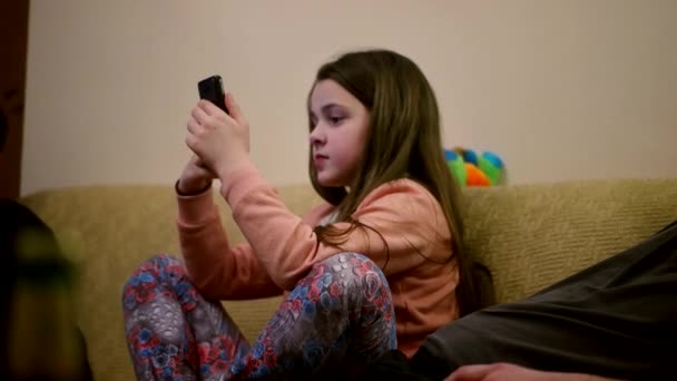 Menina bonito jogar com smartphone no sofá — Vídeo de Stock