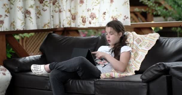 За допомогою планшетного комп'ютера, лежачи на шкіряний диван на терасі дівчина — стокове відео