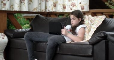 Divan terasta tablet bilgisayar kullanan küçük kız