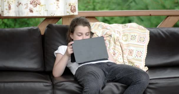 Девочка с планшетного компьютера на диване на террасе — стоковое видео