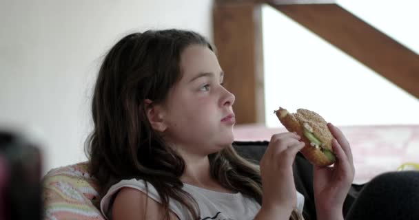 幸せな女の子がベランダで大きな食欲をそそるハンバーガーを食べる — ストック動画