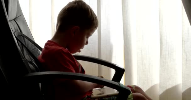 Niño usando el panel táctil mientras juega videojuegos sentado en la silla de la oficina — Vídeo de stock