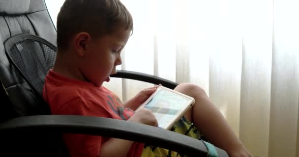 Niño usando el panel táctil mientras juega videojuegos sentado en la silla de la oficina — Vídeo de stock