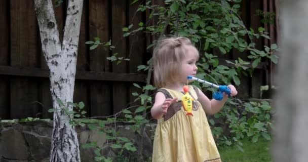 Милая девочка играет со своим набором игрушек для рыбалки на открытом воздухе — стоковое видео