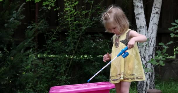 Una linda niña juega con su juguete conjunto de pesca al aire libre — Vídeos de Stock