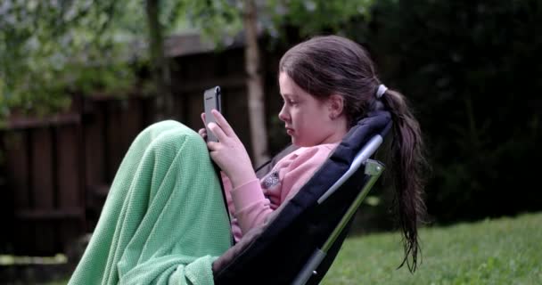 Little Girl Using Touchpad on Chair Outdoor — Stock Video