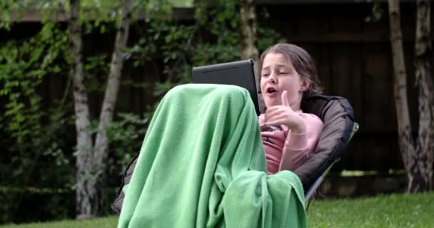 Menina usando Touchpad na cadeira ao ar livre e fazer uma cara engraçada — Vídeo de Stock