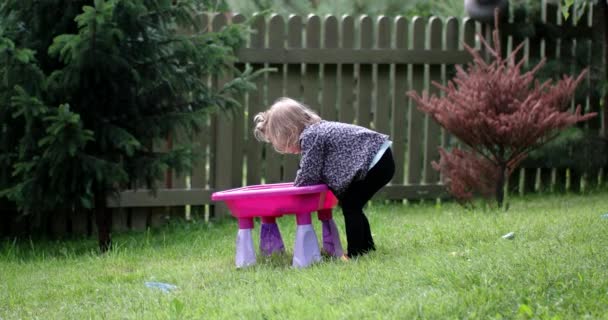 Una linda niña juega con su juguete conjunto de pesca al aire libre — Vídeo de stock