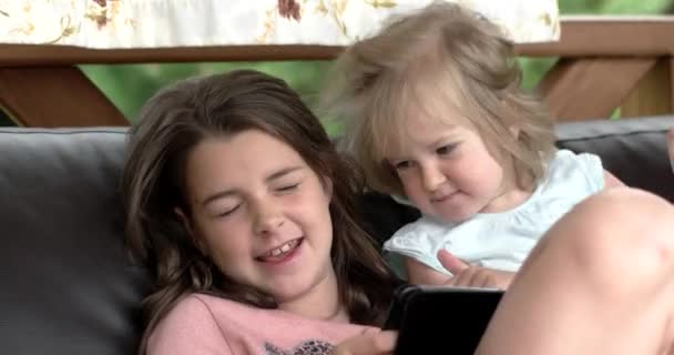 Duas meninas usando computador tablet no sofá no terraço — Vídeo de Stock