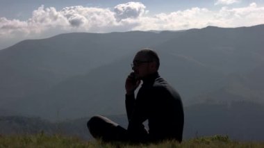 Genç adam dağın tepesinde manzara arka plan ile bir cep telefonu kullanarak