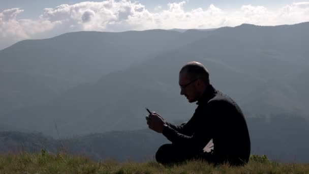 Young Man is praten op een mobiele telefoon op een berg landschap-achtergrond — Stockvideo