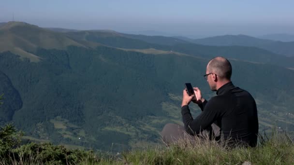 Giovane utilizzando un telefono cellulare su una cima di montagna con sfondo paesaggio — Video Stock