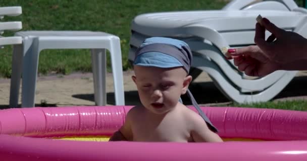 Bambino gioca e si diverte nella piscina gonfiabile sul prato verde in una giornata soleggiata — Video Stock