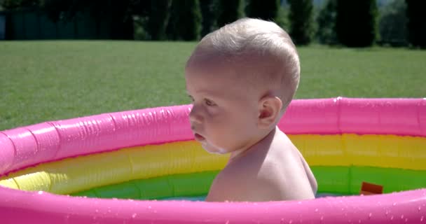 Bambino gioca e si diverte nella piscina gonfiabile sul prato verde in una giornata soleggiata — Video Stock