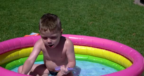 Jongen spelen en hebbend pret in opblaasbaar zwembad op groen gazon in een zonnige dag — Stockvideo