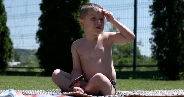 Маленький хлопчик сидить на зеленому лузі з мобільним телефоном — стокове відео