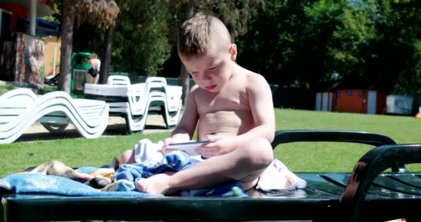 Jongen zit op een groene weide met een mobiele telefoon — Stockvideo