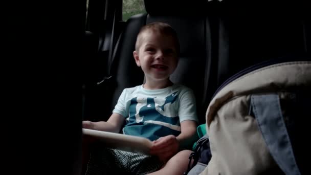 Niño pequeño usando una tableta sentada en un coche de asiento de coche — Vídeos de Stock