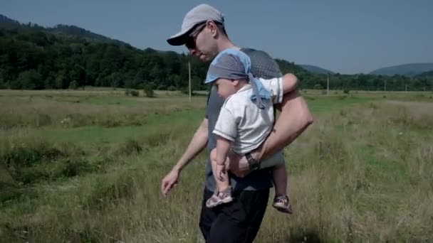 Pequeño niño siendo llevado por su padre fuera en el campo — Vídeo de stock