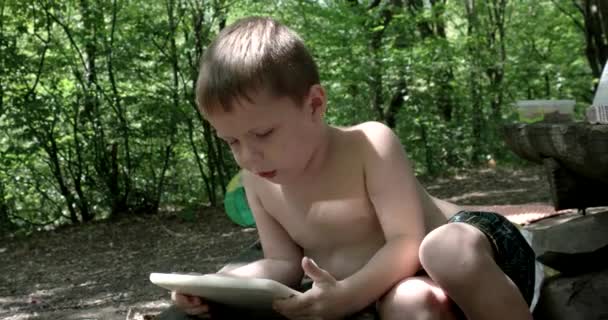 Χαριτωμένο μικρό αγόρι, χρησιμοποιώντας έναν υπολογιστή Tablet σε εξωτερικούς χώρους — Αρχείο Βίντεο