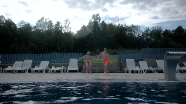 Pojke och flicka håller händer och kör tillsammans och hoppa i poolen — Stockvideo
