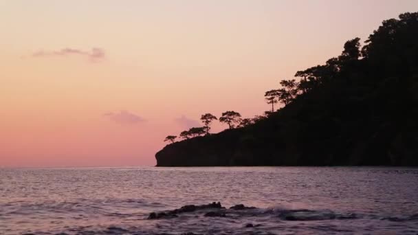 Mořské vlny a poloostrov silueta se stromy při západu slunce. — Stock video