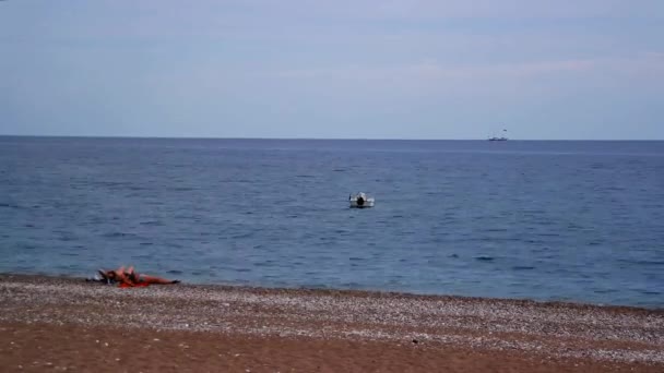 Paar ontspannen op het strand terwijl de Motor visser boot varen op zee horizon — Stockvideo