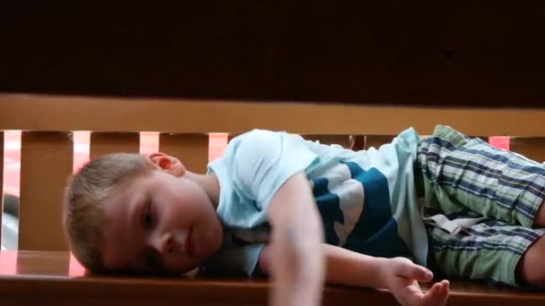 Adorable niño, acostado en un banco, sonriendo a la cámara — Vídeos de Stock