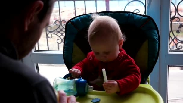 Jovem pai alimentando bebê filho em cadeira alta na cozinha — Vídeo de Stock