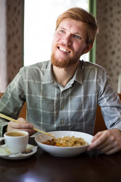 Un hombre en un café comiendo fideos asia — Foto de Stock