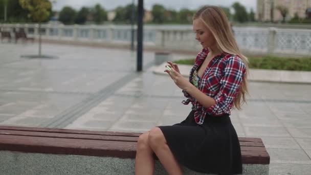 Mujer joven con teléfono inteligente sentado en un banco en el parque, disparo de cerca — Vídeo de stock