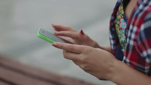 Hände junge Frau mit Smartphone sitzt auf einer Bank im Park, Nahaufnahme — Stockvideo