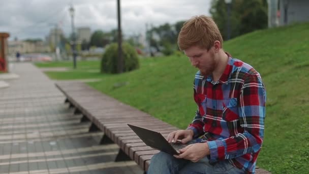 Молодой человек, работающий на ноутбуке в парке — стоковое видео