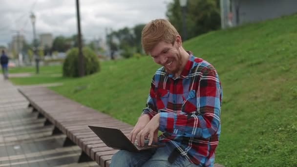 Junger Mann arbeitet im Park am Laptop — Stockvideo