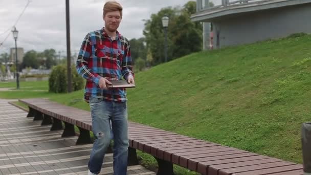 Молодой человек, работающий на ноутбуке в парке — стоковое видео