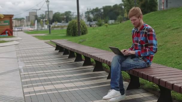 Joven trabajando en el portátil en el parque — Vídeos de Stock