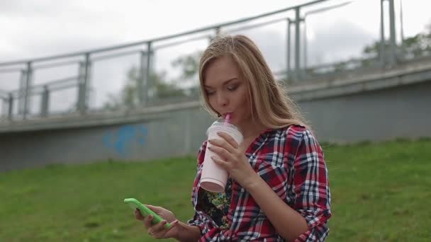 Mujer joven bebiendo un batido saludable en la calle — Vídeo de stock