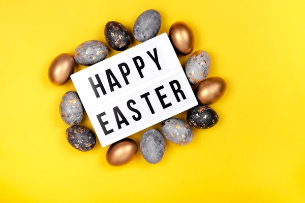Decorated with gold Easter eggs and a letter board Happy Easter on a bright yellow holiday background. Top horizontal view copyspace.