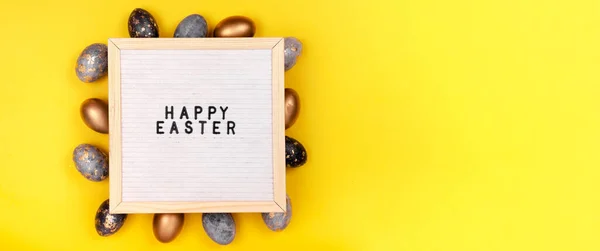 Decorated with gold Easter eggs and a letter board Happy Easter on a bright yellow holiday background. Top horizontal view copyspace.