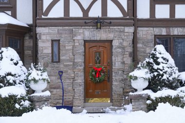 Çam çalısı ve Noel çelengi kaplı Tudor tarzı evin ön kapısı.