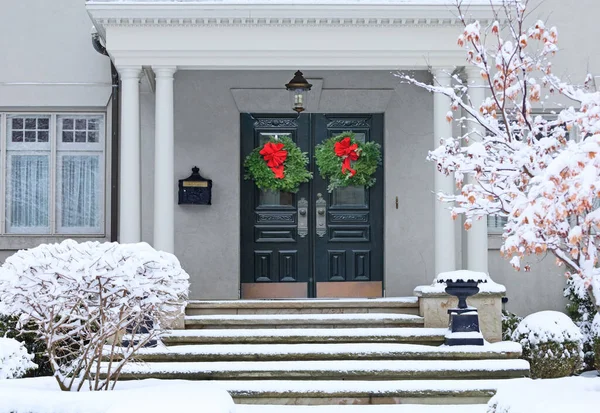 Karla kaplı evin çift ön kapısında Noel çelengi