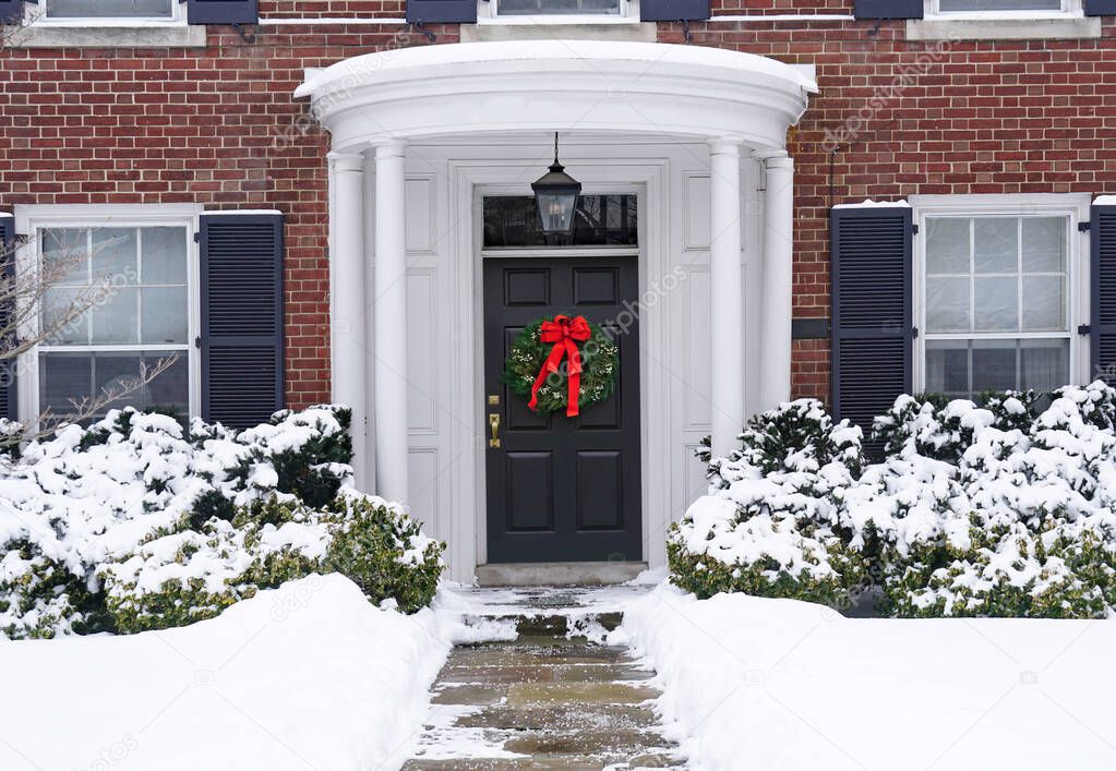 Traditional older brick home,snow covered  with portico entrance and Christmas wreath on front door