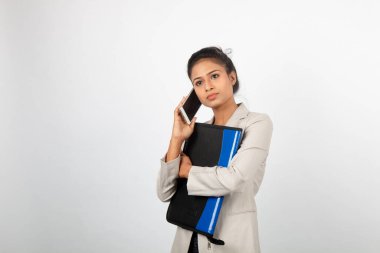 Elinde dosya ve akıllı telefon tutan neşeli bir ofis çalışanı. Resmi giyinmiş genç bir kadın beyaz arka planda beyaz ceket giyiyor..