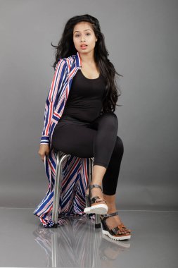 Dişi bir dansçı metal bir taburede oturur, çizgili uzun paltosu etrafında dönerken canlı ve anlamlı bir poz verir. Moda, yaşam tarzı, güçlendirme ve yaratıcı hareket kavramları için mükemmel..