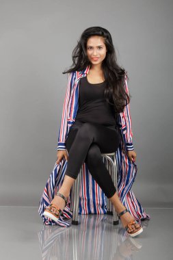 Dişi bir dansçı metal bir taburede oturur, çizgili uzun paltosu etrafında dönerken canlı ve anlamlı bir poz verir. Moda, yaşam tarzı, güçlendirme ve yaratıcı hareket kavramları için mükemmel..